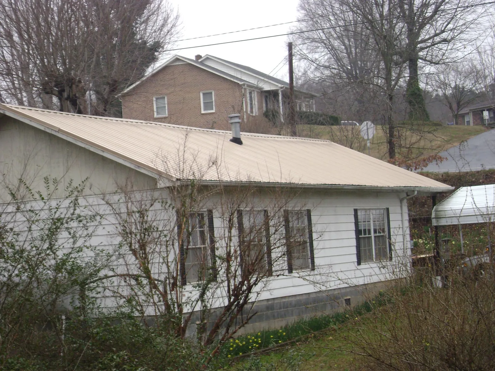 Tan metal roof on a white sided house set into a hillside — Commercial Roofing by Roofing Brothers in Shelton